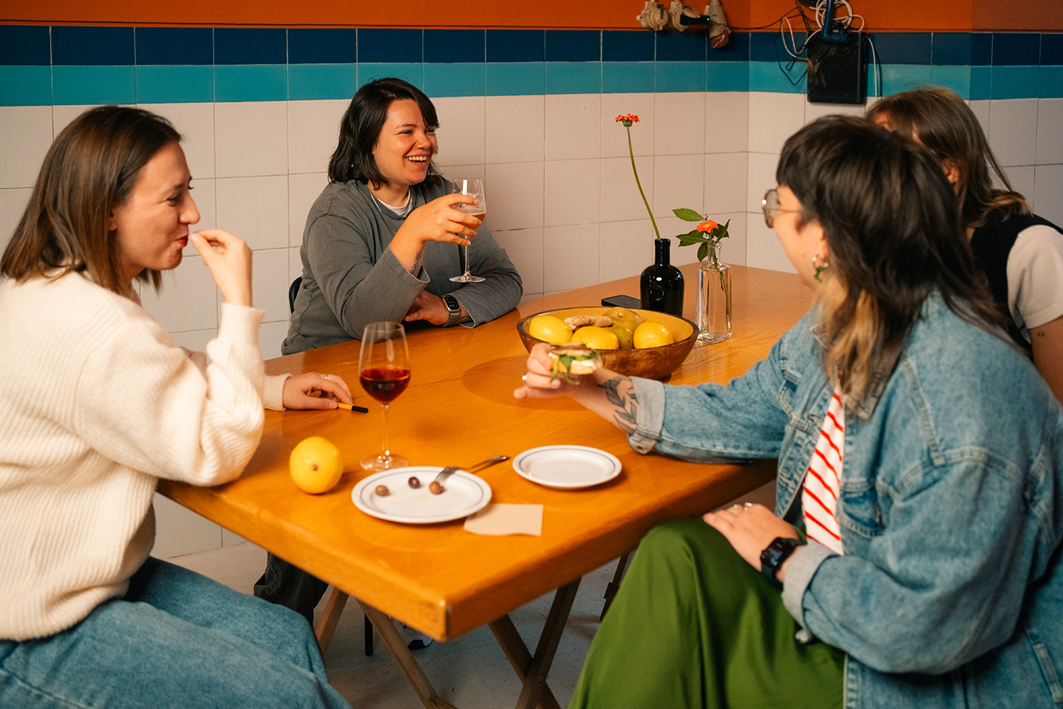 Friends Enjoying Drinks and Conversation Indoors Group of friends gathered at a wooden table, sharing drinks and enjoying a relaxed conversation in a cozy setting.