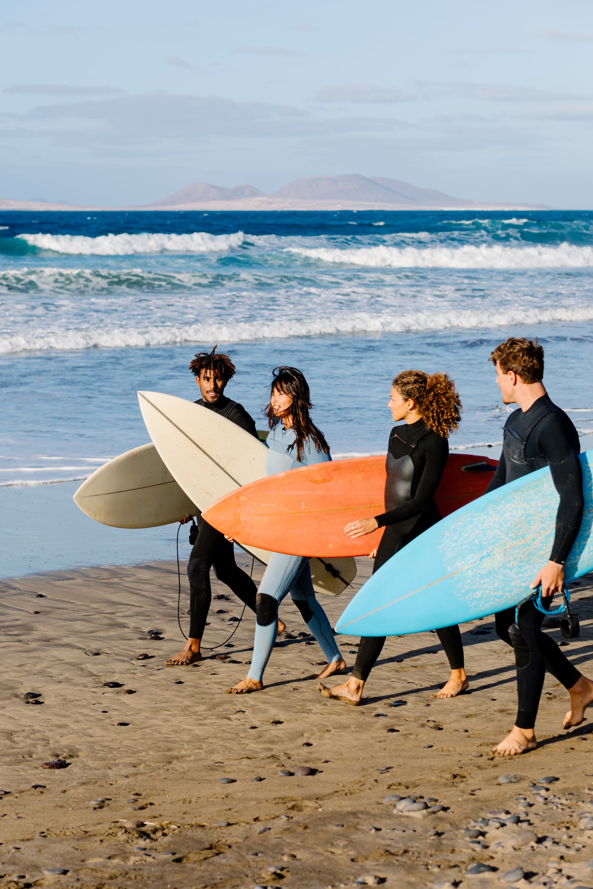 Long shot of a diverse friends walking side by side with surfboards