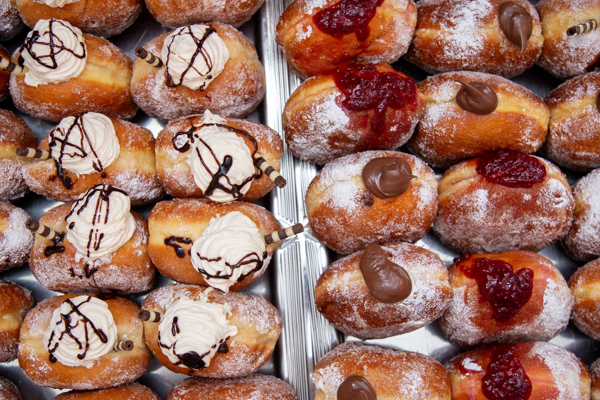 Lots of Sweet Donuts on a Tray A diverse selection of sweet donuts/doughnuts, featuring different flavors, toppings, and styles: chocolate, raspberry jam, and cream.