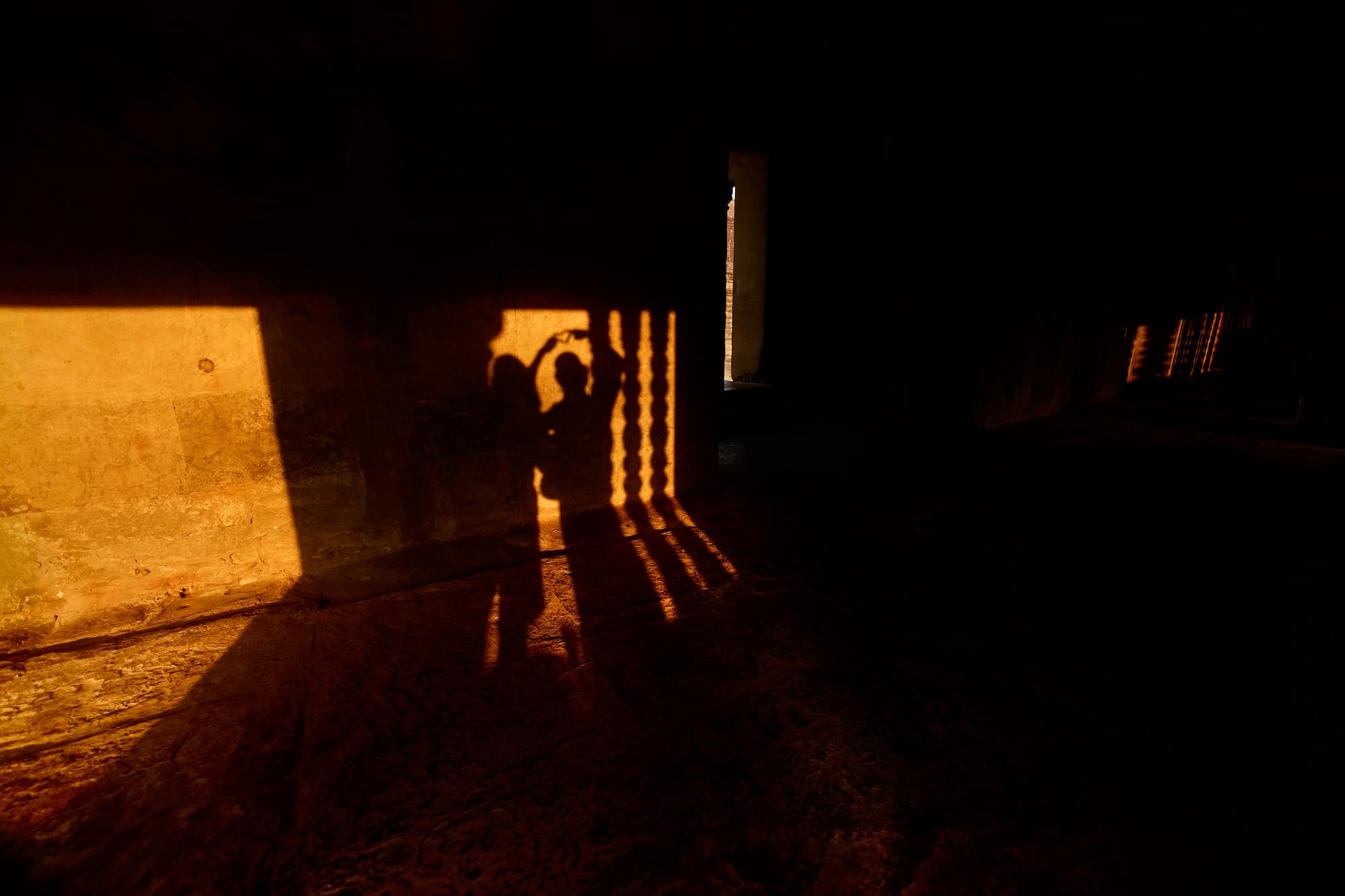 Couple playing Shadows Cast by Window at Angkor Temple Long shadows of a person and stone columns stretch across the floor at sunset inside a dark temple room in Siem Reap, Cambodia.