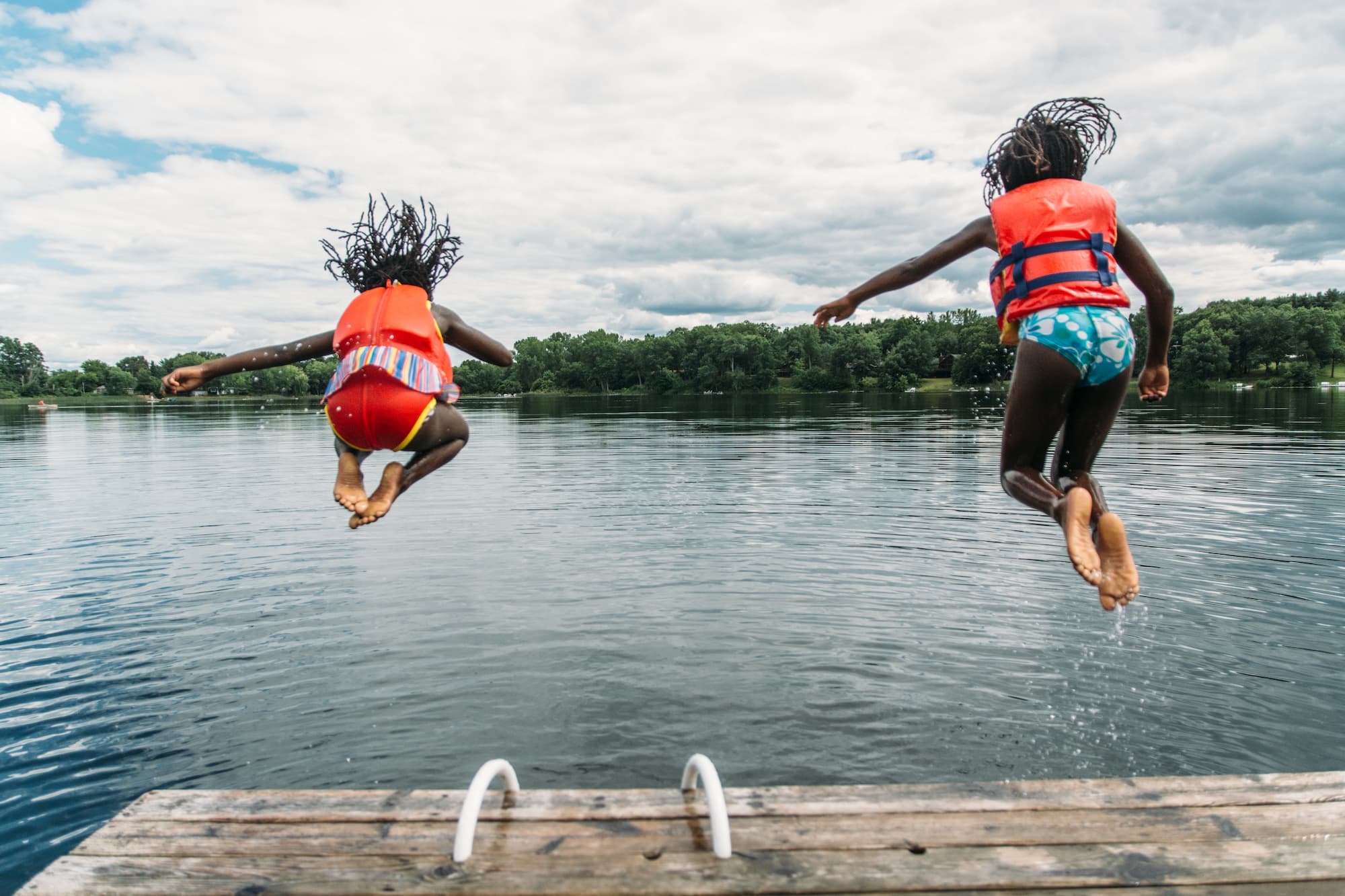 Two African-American Girls in Life Vests Jumping In A Lake