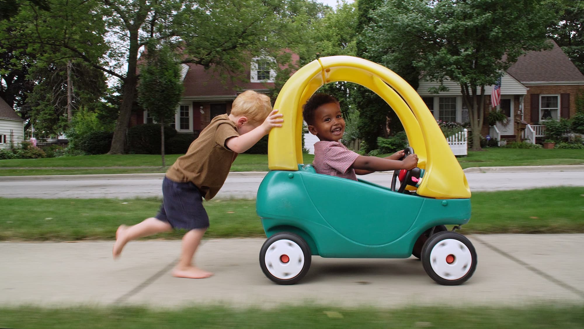 Caucasian boy playing with black boy Caucasian boy pushing a black boy in a toy car on a sidewalk