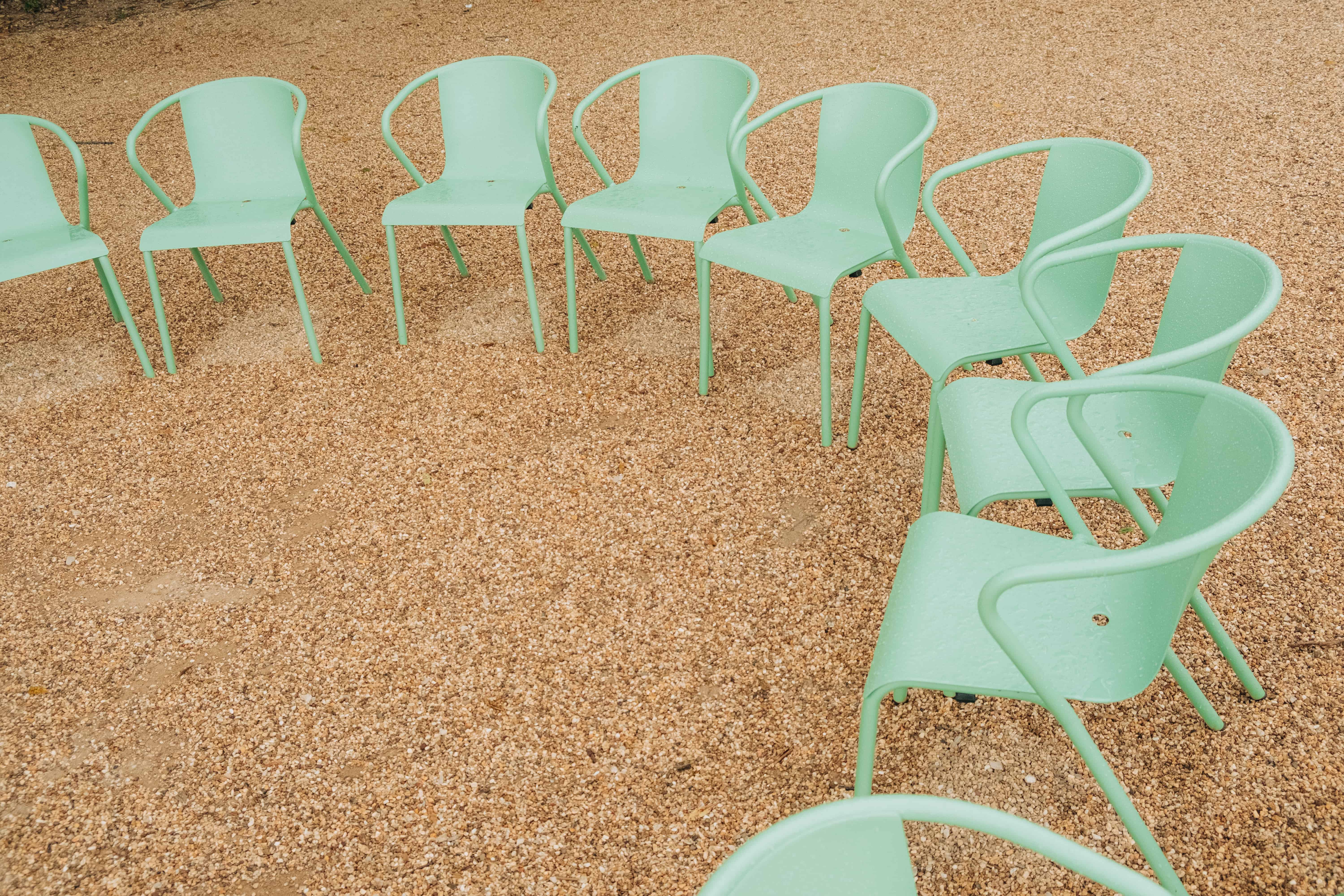 Detail shot of green chairs forming a circle on a gravel surface in an outdoor space
