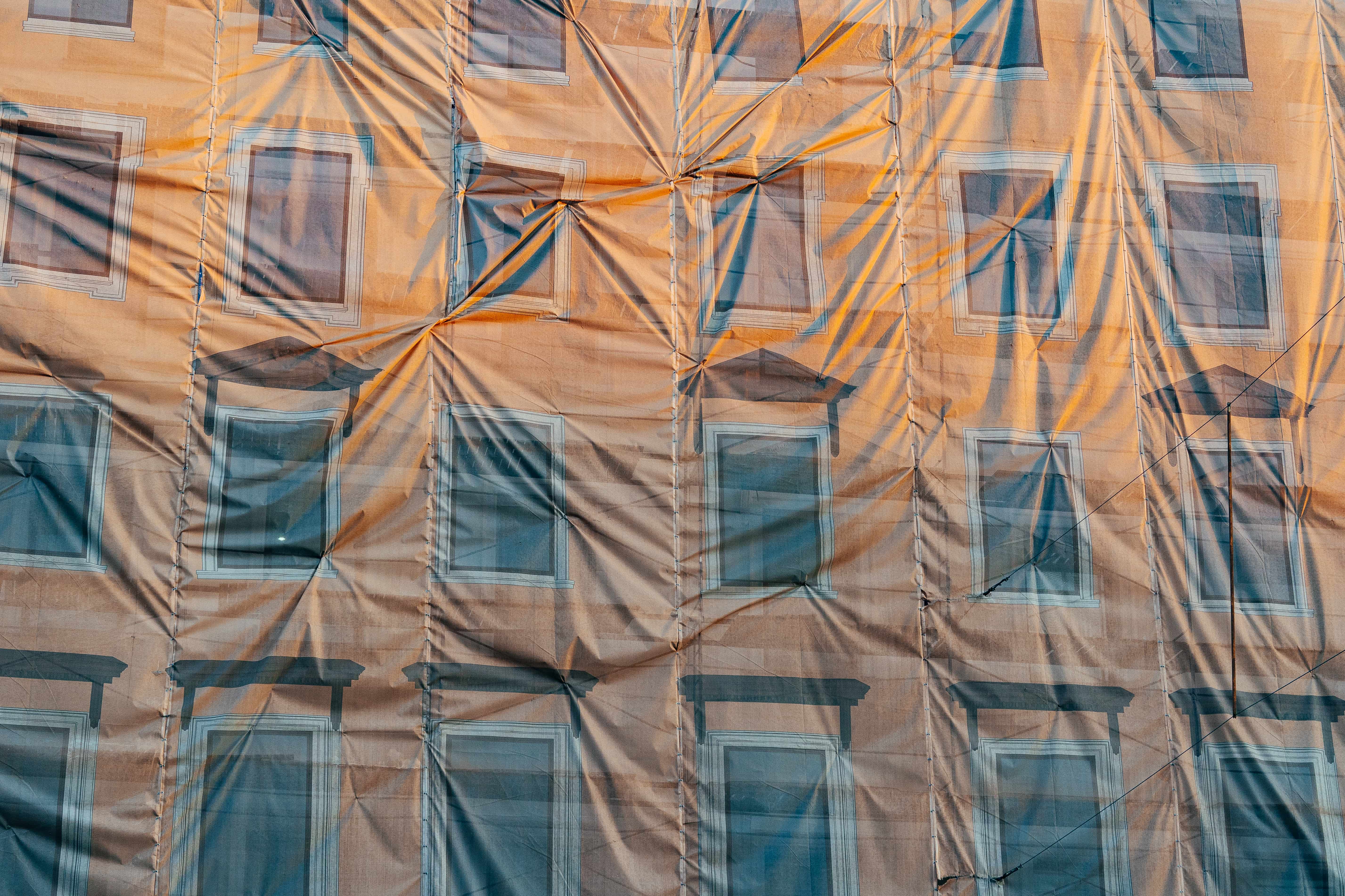 Building restoration in progress revealed through construction cover Construction workers are updating a historic building's facade. Colorful scaffolding and protective cover create an interesting visual pattern against the warm building tones at sunrise.