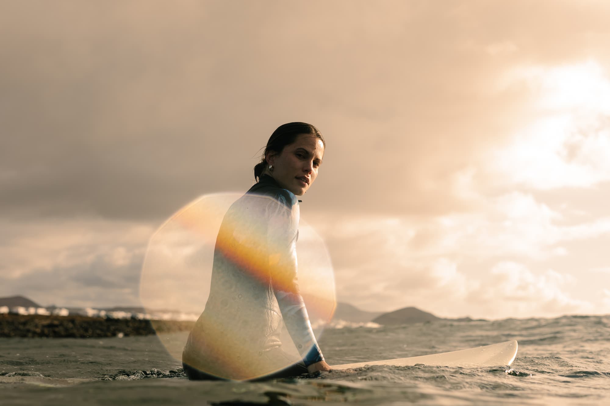 A portrait captures the joy of a professional surfer as she floats happily on her surfboard in the Atlantic Ocean at sunset.