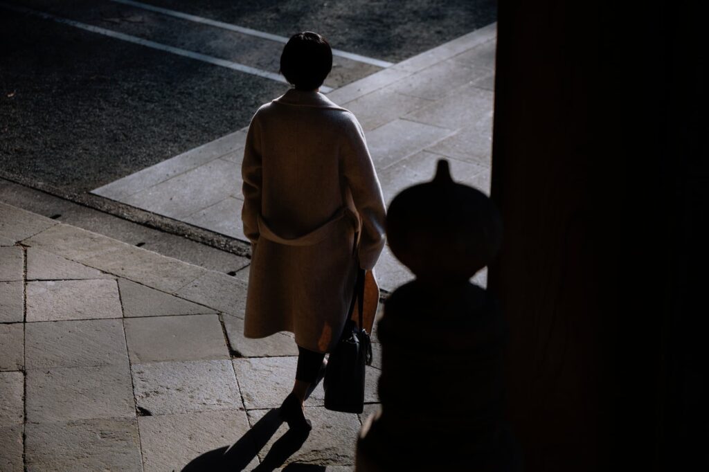 In a Japanese temple at dusk, a short-haired woman walks gently on a stone path, with the sunset's light and shadow outlining her elegant figure.