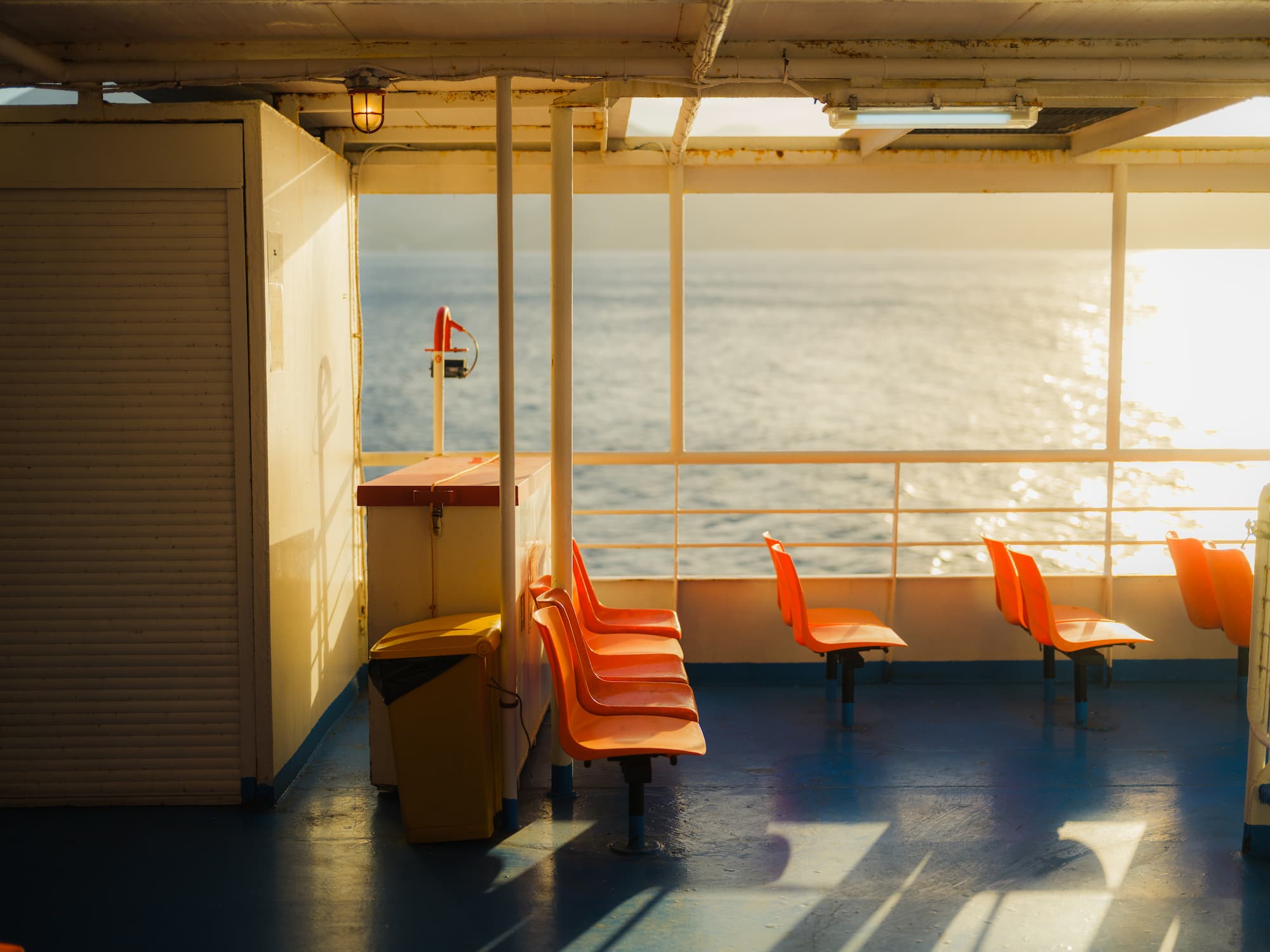 Orange plastic chairs on deck of a ferry cruising between Greek islands. Lit by warm sunset light