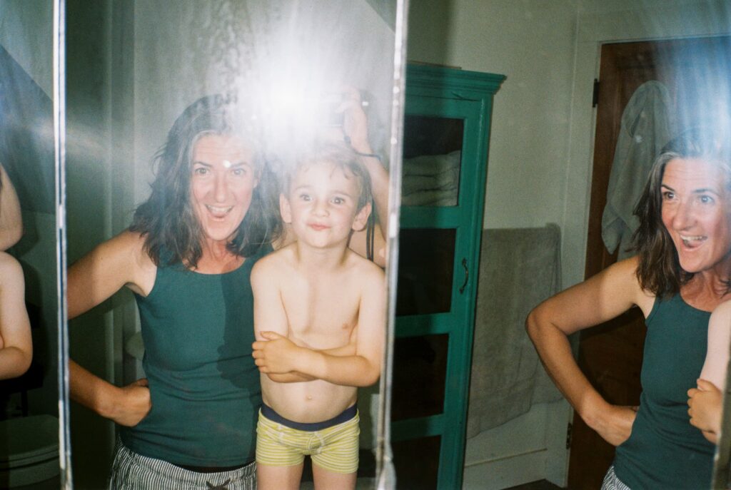 Mother and young son pose in the bathroom mirror at home. Candid family portrait captured on 35mm film with point and shoot camera.